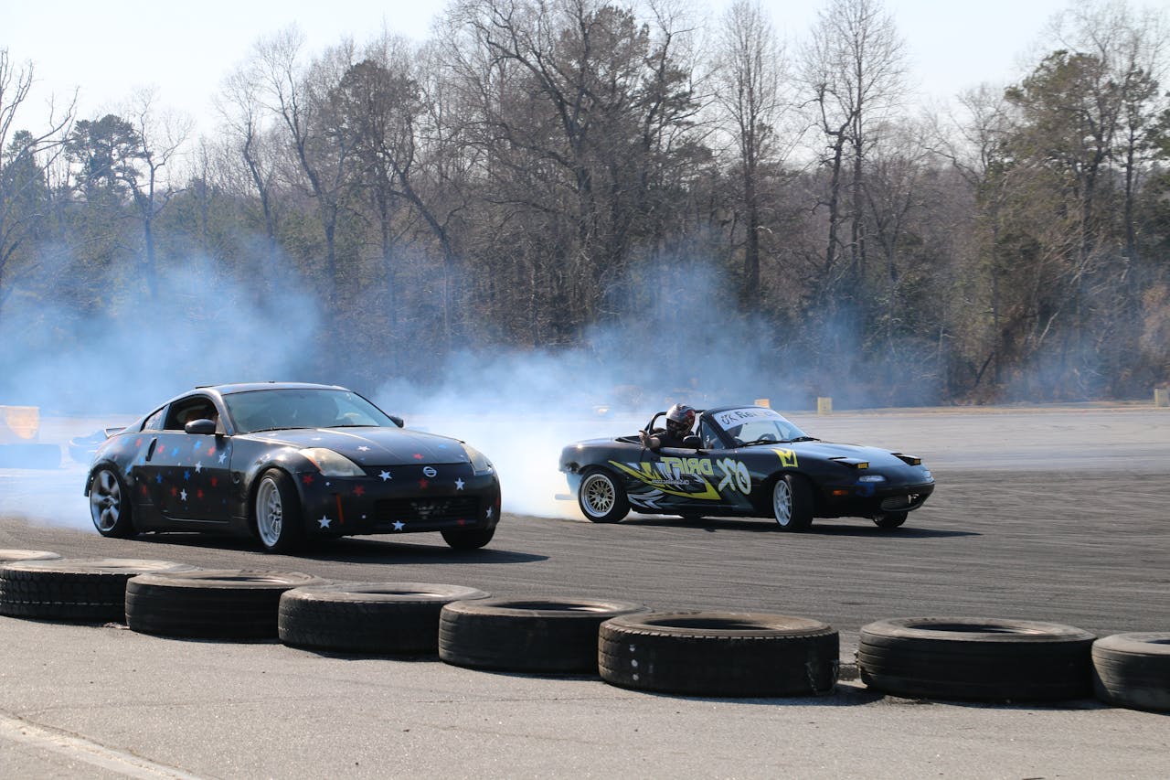 menu-12 Nissan 350Z and Mazda MX-5 cars drift fiercely on a track, leaving smoke trails.