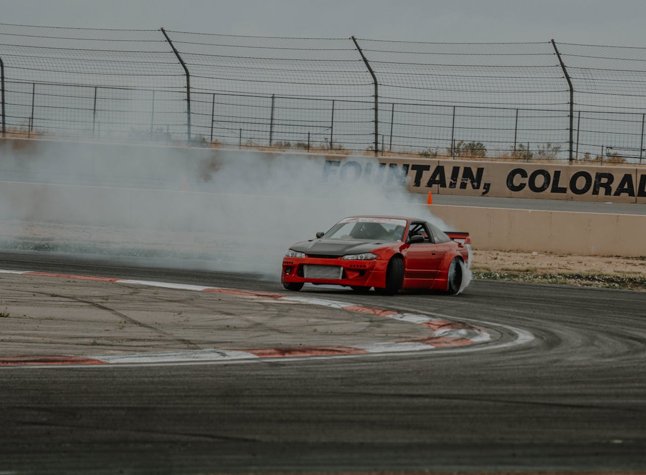 menu-07 A red Nissan Silvia drifts through a smoky turn at a Colorado race track, showcasing skillful automotive control.