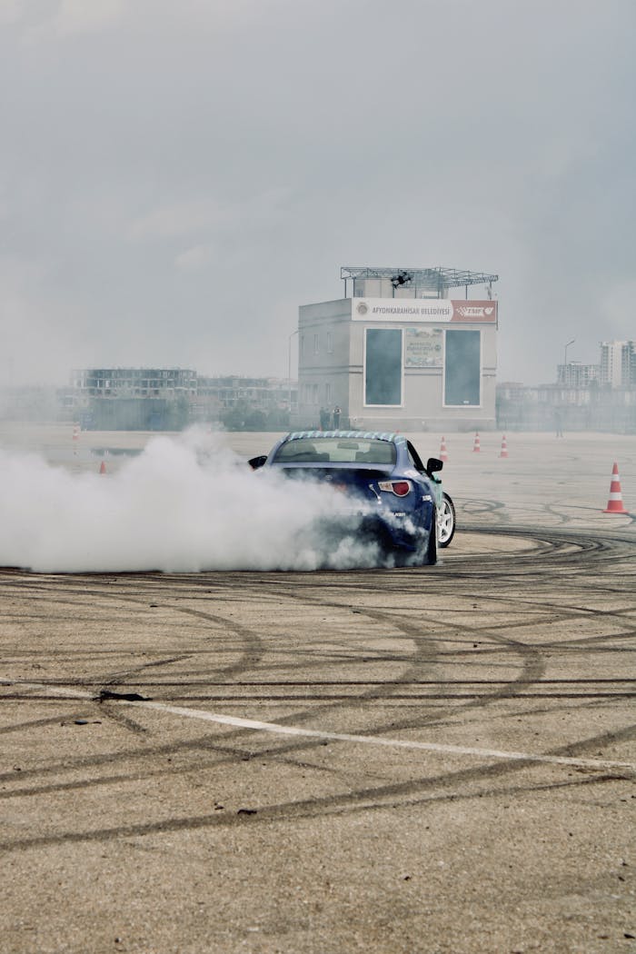 menu-06 Blue car performing drift on a race track surrounded by tire smoke.