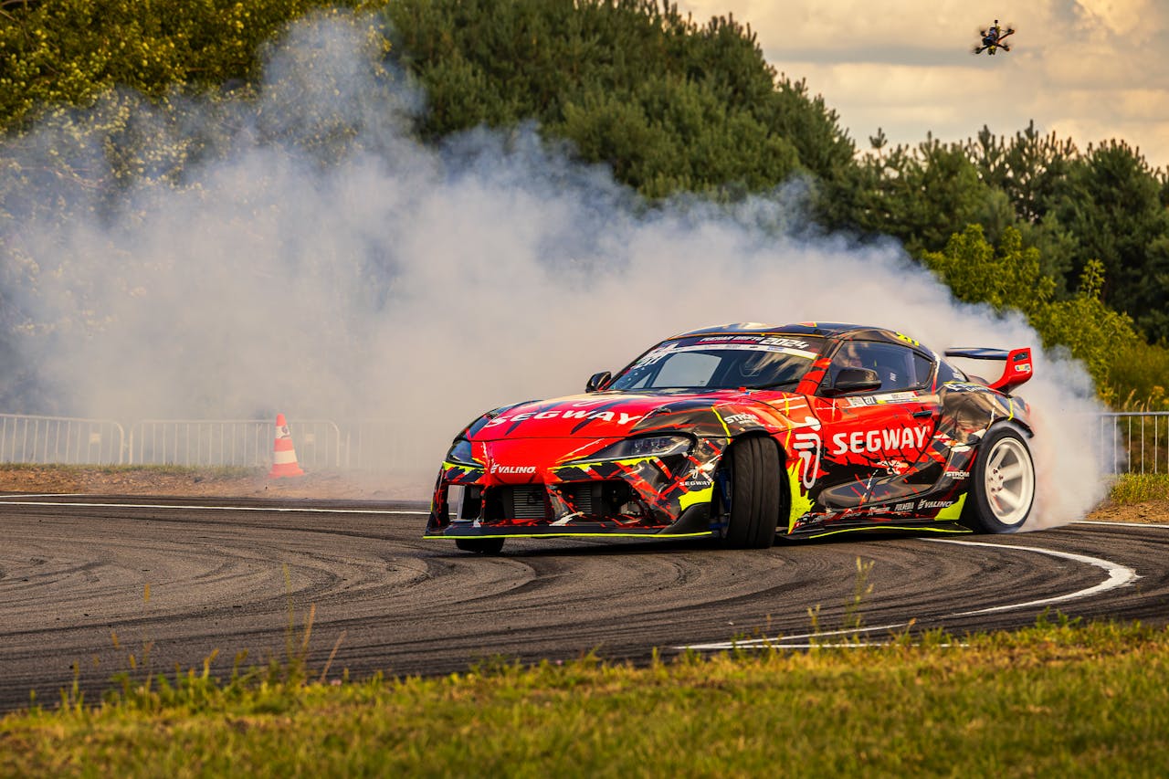 menu-01 A dynamic car drifts with smoke on a race track surrounded by nature, capturing speed and power.